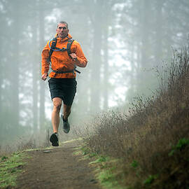Man Trail Running In The Woods And Fog by Corey Rich