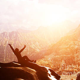 A happy man sitting on the peak of a mountain with hands raised at sunset by Michal Bednarek