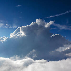 Blue sky background with white clouds with sun in frame by Sarah Fields