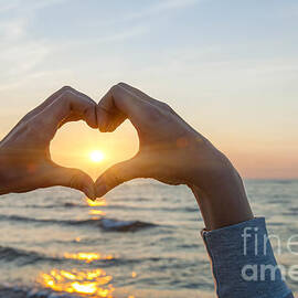 Fingers heart framing ocean sunset