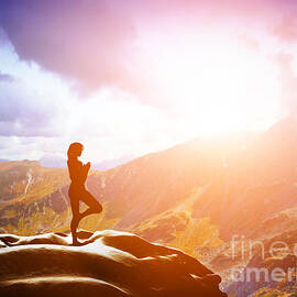 Woman standing in tree yoga position meditating in mountains at sunset by Michal Bednarek