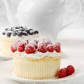 Cupcakes with rasberries and cream on table by Sandra Cunningham