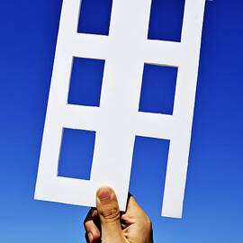 Hand holding house shape on blue sky by Sami Sarkis Photography