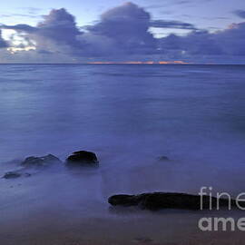 Tree trunk and rocks partially submerged in sea at sunrise by Sami Sarkis Photography