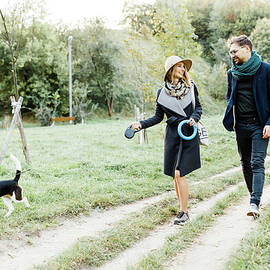 Couple Is Walking In The Park Playing With A Beagle Dog Having Fun by Cavan Images / Orest Filin