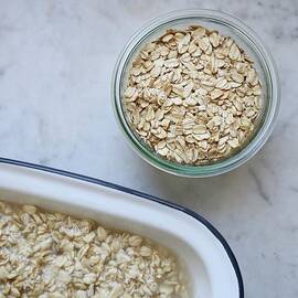 A Jar Of Organic Oats And Softened Oats In An Enamel Dish On A Marble Surface by Bayle Doetch