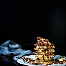A Stack Of Banana Pancakes With Roasted Pecans, Banana Slices And Nutella Sauce by Lisa Rees