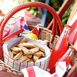 Cantucci Biscuits In Biscuit Tin With Glass Bottles Of Juice In Picnic Basket by Brett Stevens