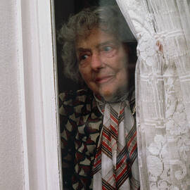 Elderly Lady Peering Out Of House Window by Science Photo Library