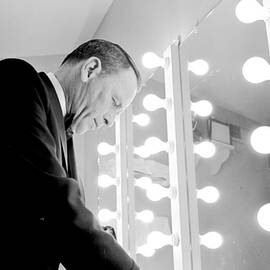 Frank Sinatra standing in front of a mirror sorting through music and notes in his dressing room at a performance. by John Dominis