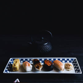 High Angle View Of Various Sushi Arranged In Plate With Chopsticks And Teapot On Table Against Black Wall by Cavan Images