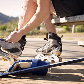 Low Section Of Man Putting On Inline Skates On Field by Cavan Images