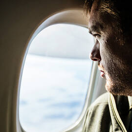 Man With Beard Looks Out The Window Of An Airplane. by Cavan Images