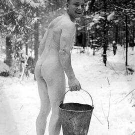 Naked Finnish soldier carrying a bucket of water back to his friends who are enjoying a sauna bath nearby. by Carl Mydans