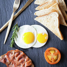 Overhead View Of Toast With Bacon, Fried Eggs And Tomato Breakfast On Slate by Luka Storm