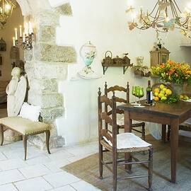 Simple Dining Table And Chairs In Front Of Open Fireplace In Open-plan Interior With View Of Bed Through Open Doorway by Blickpunkte