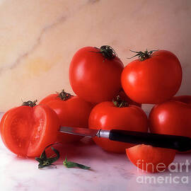  Ripe tomatoes on a table which one of them is cut with a knife in it by BERNARD JAUBERT