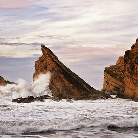 Sunset glow on the sandstone cliffs and crashing waves at Shore Acres State Park. by Larry Geddis