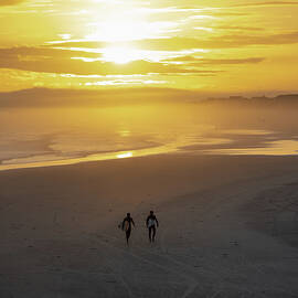 Two Surfers Walking On Shoreline at Sunset by Good Focused