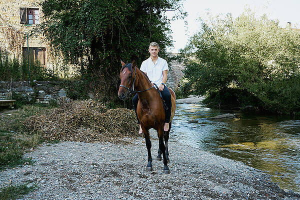 Wall Art - Photograph - Portrait Of A Young Blond Man Riding A Horse Over A River #1 by Cavan Images