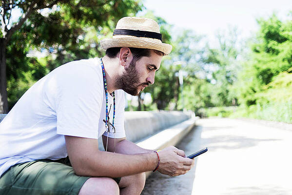 Wall Art - Photograph - Smiling Young Bearded Man Sitting On Bench Using A Smartphone by Cavan Images