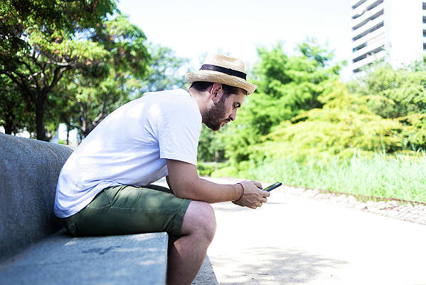 Wall Art - Photograph - Smiling Young Bearded Man Sitting On Bench Using A Smartphone by Cavan Images