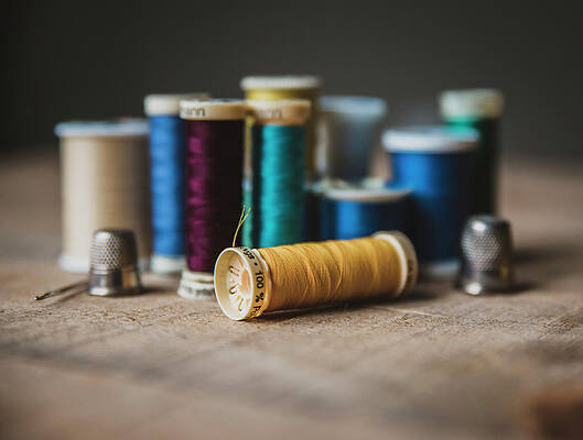 Wall Art - Photograph - Close-up Of Colorful Spools With Thimbles On Wooden Table At Workshop by Cavan Images