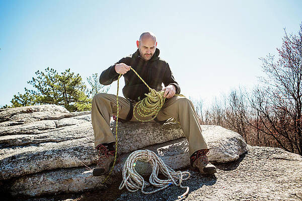 Wall Art - Photograph - Hiker With Rope Preparing For Rappelling While Sitting On Rocks Against Clear Sky by Cavan Images