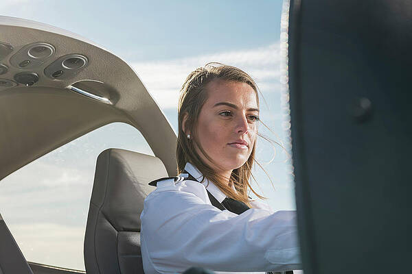 Wall Art - Photograph - Low Angle View Of Female Pilot Operating Control Panel While Sitting In Airplane Against Blue Sky At Airport by Cavan Images