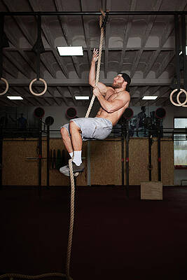 Wall Art - Photograph - Man Climbing On Rope While Exercising In Gym by Cavan Images