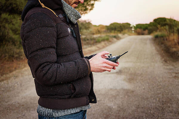 Wall Art - Photograph - Midsection Of Man Operating Drone's Remote Control While Standing On Dirt Road by Cavan Images