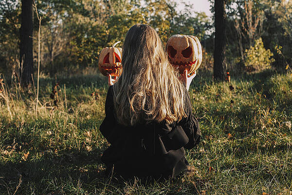 Wall Art - Photograph - Rear View Of Woman Holding Jack O' Lanterns While Sitting On Grassy Field In Forest During Halloween by Cavan Images