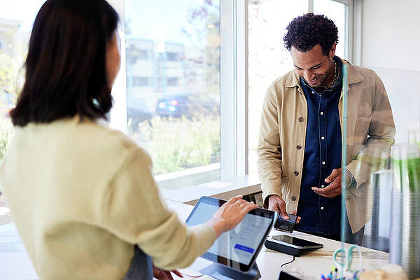 Wall Art - Photograph - Smiling Man Paying Through Smart Phone By At Checkout Counter In Cafe by Cavan Images / Jack Jeffries
