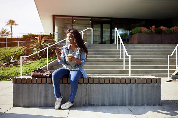 Wall Art - Photograph - Smiling Woman Using Smart Phone While Sitting On Bench by Cavan Images / Jack Jeffries