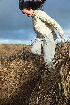 Wall Art - Photograph - Woman Running Down Hill With Tall Grass As The Wind Blows In Denmark by Cavan Images