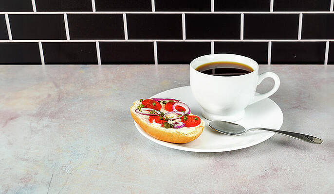 Wall Art - Photograph - Coffee and bagel on white on pink tinged countertop with black subway tile background. by Mike Worley