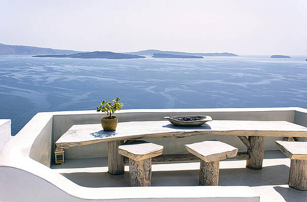 Wall Art - Photograph - Santorini, A pot with flower or plant and a plate on a wooden table with wooden chair against beautiful sea ocean background with mountains by Arpan Bhatia
