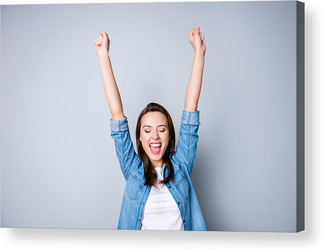 Working Acrylic Print featuring the photograph Amazed brunette young business woman in casual shirt is gesturing victory with her raised hands, she is shocked, extremely happy, with closed eyes, beaming smile, open mouth on grey background by Deagreez