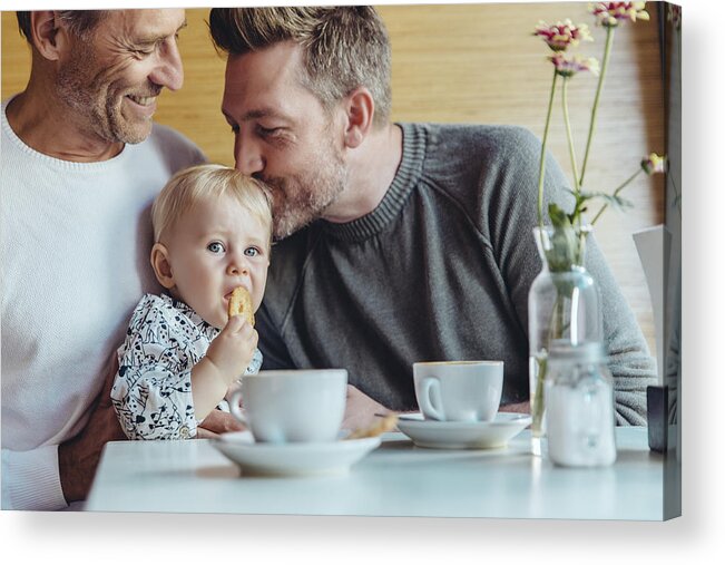 Mature Adult Acrylic Print featuring the photograph Gay couple cuddling with their baby in cafe by Westend61