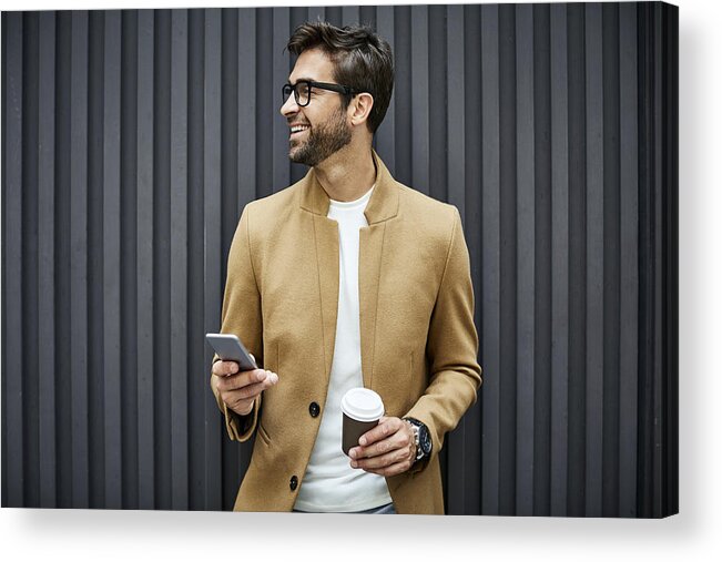 Handsome People Acrylic Print featuring the photograph Smiling businessman with smart phone and cup by Morsa Images