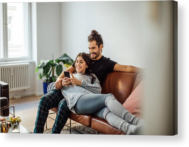 Young Men Acrylic Print featuring the photograph Young couple with mobile phone relaxing on sofa by Luis Alvarez
