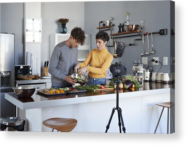Domestic Room Acrylic Print featuring the photograph Two food vloggers making video while prepping vegetables in kitchen #1 by Klaus Vedfelt