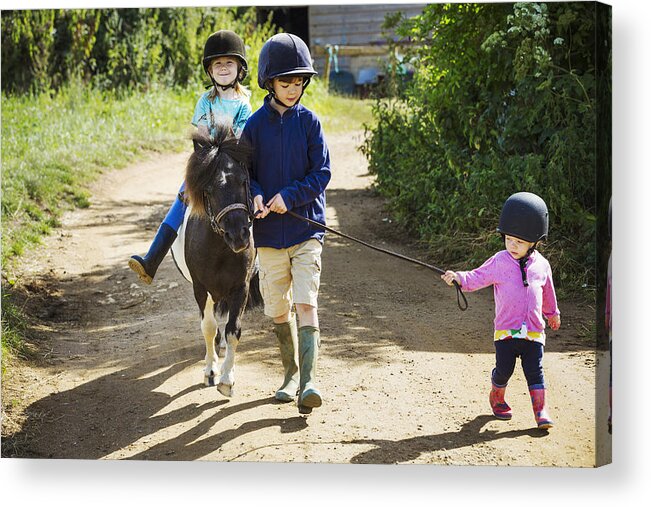 Horse Acrylic Print featuring the photograph A boy, a toddler, and a girl riding a pony on a dirt path. by Mint Images