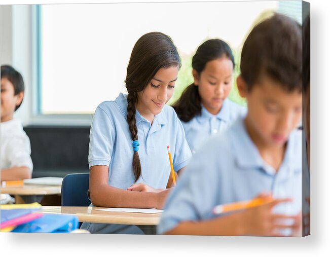 Working Acrylic Print featuring the photograph Hispanic schoolgirl concentrates while working on class assignment by SDI Productions