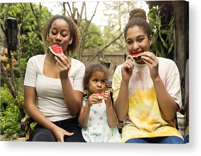Diversity Acrylic Print featuring the photograph Mixed-race sisters eating watermelon in backyard. by Martinedoucet
