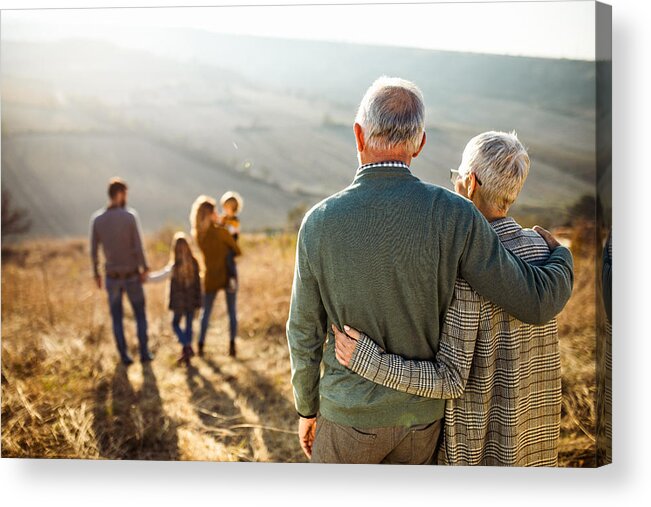 Heterosexual Couple Acrylic Print featuring the photograph Rear view of embraced senior couple looking at their family in nature. by Skynesher