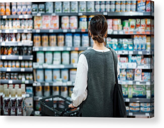 Confusion Acrylic Print featuring the photograph Rear view of young Asian mother with a shopping cart grocery shopping for baby products in a supermarket. She is standing in front of the baby product aisle and have no idea which product to choose from by D3sign