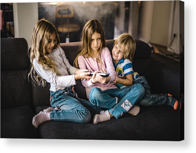 Problems Acrylic Print featuring the photograph Small siblings fighting over a remote control in the living room. by Skynesher