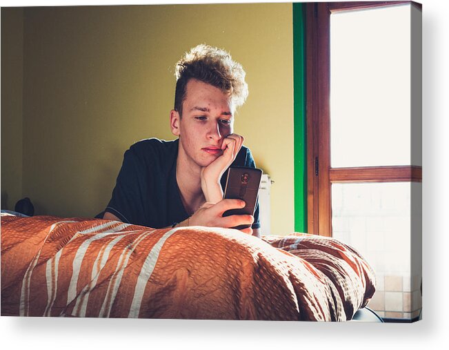 Telephone Acrylic Print featuring the photograph Teenage Boy Using his Smart Phone while Laying on the Bed by CasarsaGuru