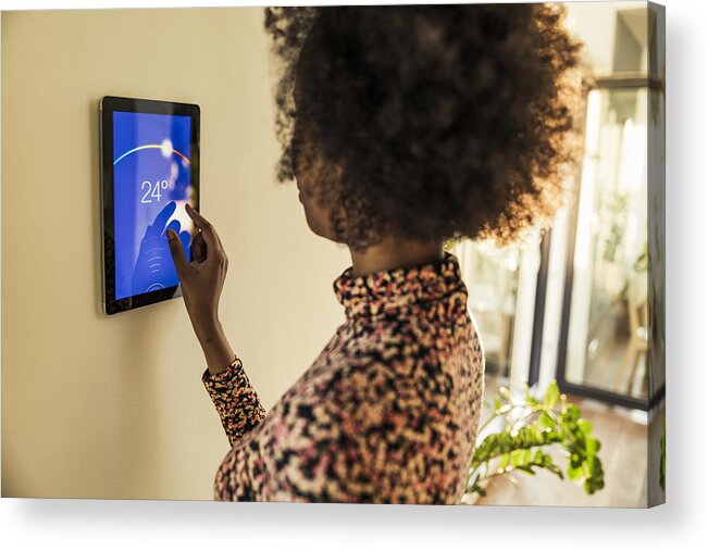 20-29 Years Acrylic Print featuring the photograph Woman adjusting temperature on smart thermostat at home by Westend61